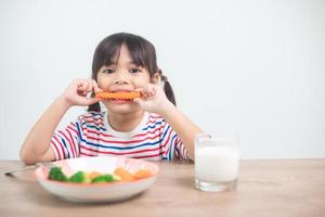 süßes asiatisches Mädchen, das gesundes Gemüse und Milch für ihre Mahlzeit isst foto