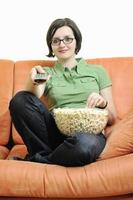 Junge Frau isst Popcorn auf orangefarbenem Sofa foto