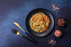 Frischer Salat aus geschnittenen dünnen Karotten- und Zucchinistreifen auf Betongrund foto
