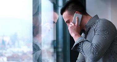 Geschäftsmann, der am Handy spricht und aus dem Bürofenster schaut foto