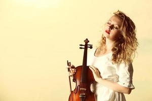 das blonde Mädchen mit einer Geige im Freien foto