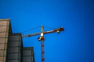 Baukran gegen den blauen Himmel. die Immobilienwirtschaft. Ein Kran verwendet Hebezeuge auf einer Baustelle. foto