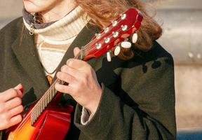 Ein junger männlicher Gitarrist sitzt auf einer Stadtstraße und spielt Mandoline. foto