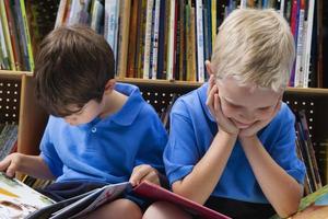 zwei Kinder, die blaue Hemden tragen, die in einer Bibliothek lesen foto