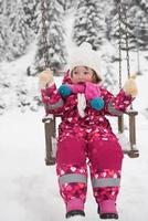 kleines Mädchen am Tag des verschneiten Winters Schaukel im Park foto