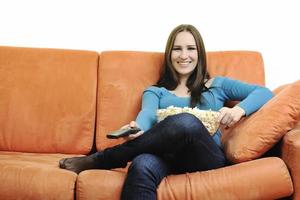 Junge Frau isst Popcorn auf orangefarbenem Sofa foto