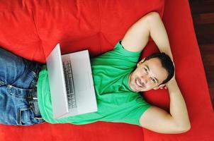 Mann entspannt sich auf dem Sofa und arbeitet am Laptop foto