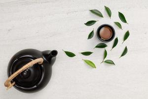 tasse heißen tee mit teekanne, grünen teeblättern und getrockneten kräutern draufsicht auf den leeren raum des weißen steintisches, organisches produkt aus der natur für gesundes mit traditionellem stil foto