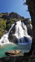 Bergwasserfall in einer felsigen Schlucht, die mit grünem Wald bewachsen ist. Strom von eisigem Wasser fällt auf moosige Steine. foto