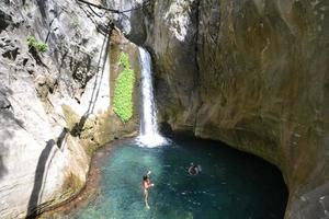 Bergwasserfall in einer felsigen Schlucht, die mit grünem Wald bewachsen ist. Strom von eisigem Wasser fällt auf moosige Steine. foto