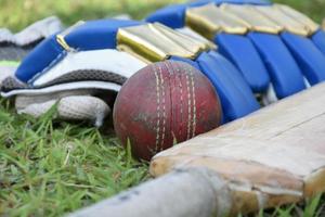 cricket-sportgeräte fledermausballhandschuhe auf grünem rasen verschwommenes grünes gras-cricketfeld, konzept für die verwendung von cricket-sportgeräten im training. foto