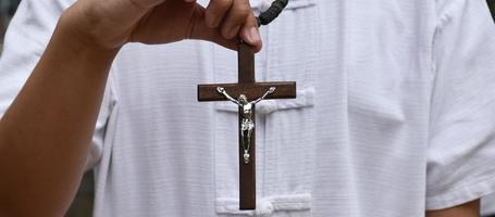 holzkreuz und holzrosenkranz werden in den händen des jungen asiatischen katholischen gebets gehalten, während sie im tempelparkbereich beten. foto