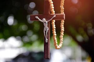 hängende Holzkreuzperlenkette, natürlicher Unschärfe-Bokeh-Bäume-Hintergrund, weicher und selektiver Fokus. foto