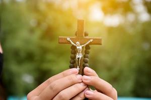 holzkreuz und holzrosenkranz werden in den händen des jungen asiatischen katholischen gebets gehalten, während sie im tempelparkbereich beten. foto