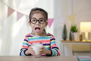 Kind asiatisches Mädchen, das etwas Milch auf dem Schreibtisch trinkt, komfortables Konzept für Kinder zu Hause foto