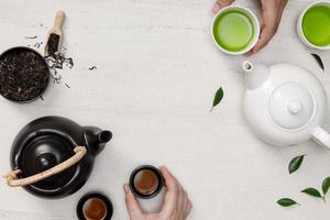 hände, die heißen dampfenden tee in der tasse mit teekanne und getrocknetem kräutertee auf dem weißen steintisch halten leerer raum kreative flachlage, organisches produkt aus der natur für gesundes mit traditionellem stil foto