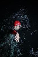 echter triathlonsportler, der in dunkler nacht schwimmt foto