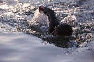 Triathlon-Athlet, der bei Sonnenaufgang auf dem See schwimmt und einen Neoprenanzug trägt foto