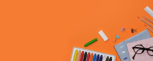 kreatives flatlay der bildung orangefarbener tisch mit schülerbüchern, bleistift, bunter kreide, brille, leerer raum in studioaufnahme isoliert auf orangefarbenem langem bannerhintergrund, bildungskonzept foto