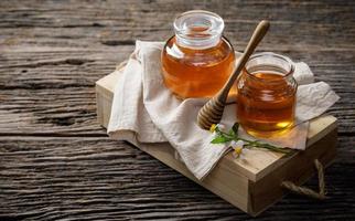 honigbiene im glas mit honiglöffel und blume auf holztisch, bienenprodukte nach bio-naturzutaten-konzept, kopierraum für ihren text foto