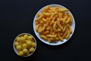 Mais gesalzen und gepfefferte Chips auf einem weißen Teller. leckeres Frühstück mit Maischips auf schwarzem Hintergrund. foto