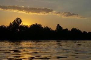 atmosphärischer sonnenuntergang hinter bäumen und reflexion im wasser. foto