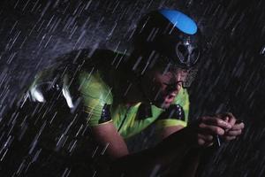 Triathlon-Athlet, der in regnerischer Nacht schnell Fahrrad fährt foto