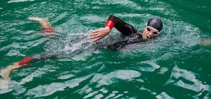 Triathlon-Athlet, der auf dem See schwimmt und einen Neoprenanzug trägt foto