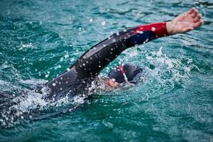 Triathlon-Athlet, der bei Sonnenaufgang auf dem See schwimmt und einen Neoprenanzug trägt foto