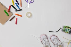 kreatives Flatlay des weißen Bildungstisches mit Schülerbüchern, Schuhen, buntem Buntstift, Kamera, leerem Raum isoliert auf weißem Hintergrund, Bildungskonzept und zurück zur Schule foto