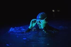 Authentischer Triathlet-Schwimmer, der während des harten Trainings im nächtlichen Neon-Gel-Licht eine Pause macht foto