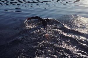 Triathlon-Athlet, der bei Sonnenaufgang auf dem See schwimmt und einen Neoprenanzug trägt foto