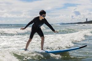 Ein kleiner Junge mit Schwimmbrille steht auf einem weichen Brett, während er in einem Anfängerkurs das Surfen übt. foto