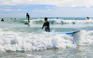 Ein kleiner Junge, der eifrig einen Badeanzug und eine Schutzbrille trägt, übt das Surfen. foto