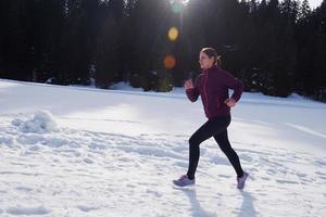 Junge Frau, die im Freien auf Schnee im Wald joggt foto