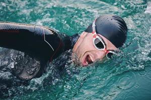 Triathlon-Athlet, der bei Sonnenaufgang auf dem See schwimmt und einen Neoprenanzug trägt foto