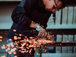 schwerindustrie-fabrikinnenraum mit industriearbeiter, der winkelschleifer verwendet und ein metallrohr schneidet. Auftragnehmer in der Herstellung von Metallstrukturen für Sicherheitsuniformen und Schutzhelme. foto