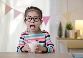 Kind asiatisches Mädchen, das etwas Milch auf dem Schreibtisch trinkt, komfortables Konzept für Kinder zu Hause foto