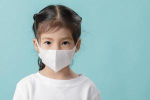 asiatisches kleines kind, das atemschutzmaske trägt, um den ausbruch des coronavirus zu stoppen, neues virus covid-19 aus dem wuhan-china-konzept, leerer raum isoliert auf blauem hintergrund foto