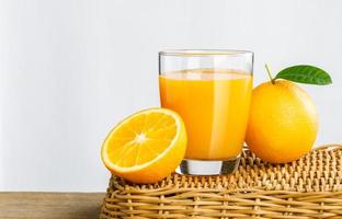 Glas frisch gepresster Orangensaft auf einem Korb, Orangensaft aus frischen Früchten im Glas mit Orangengruppe auf weißem Hintergrund, selektiver Fokus auf Glas, isolierter weißer Hintergrund foto