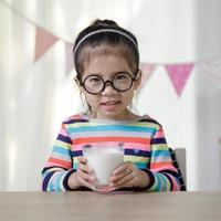 Kind asiatisches Mädchen, das etwas Milch auf dem Schreibtisch trinkt, komfortables Konzept für Kinder zu Hause foto