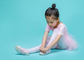 schöne lächelnde asiatische kleine Mädchen in einem rosafarbenen Anzug tanzt ein Ballett in der Schule, leerer Raum in Studioaufnahme isoliert auf buntem blauem Hintergrund foto