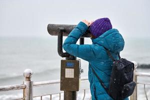 Frau, die im Winter durch Fernglas auf See schaut foto