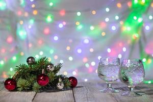 zwei gläser weihnachtschampagner mit weihnachtsbaum, der aus roten und silbernen kugeln vor hellem bokeh-hintergrund geschmückt ist foto