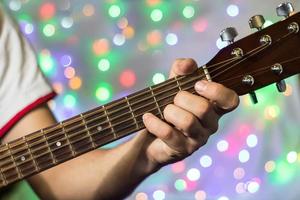 Mann spielt auf Akustikgitarre. Closeup Finger am Gitarrenhals gegen Weihnachten verschwommene Bokeh-Lichter im Hintergrund foto