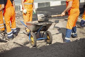 Reparatur der Straße. Verlegen von Asphalt auf der Straße. Arbeiter in orangefarbener Kleidung. foto