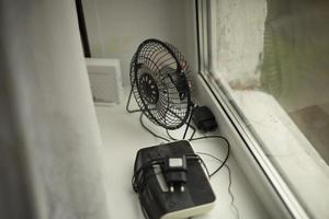 Ventilator ist am Fenster. Gegenstände liegen auf der Fensterbank. Elektrogeräte zu Hause. foto