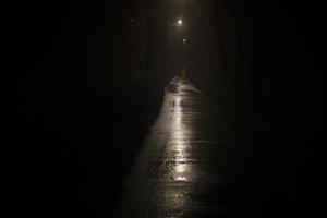 licht in der nacht im park. Licht auf nasser Fahrbahn im Dunkeln. Es ist ein unheimlicher Park. foto