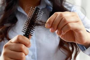 rückansicht junge frau besorgt über haarausfallproblem, hormonelles ungleichgewicht, stresskonzept. Viele Haare fallen nach dem Kämmen in der Haarbürste in der Hand aus. Weibchen entwirrt ihr Haar mit einem Kamm, Gesundheitsversorgung foto