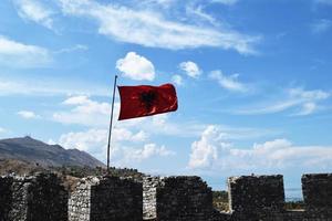 die flagge albaniens gegen den blauen himmel schwenkend foto